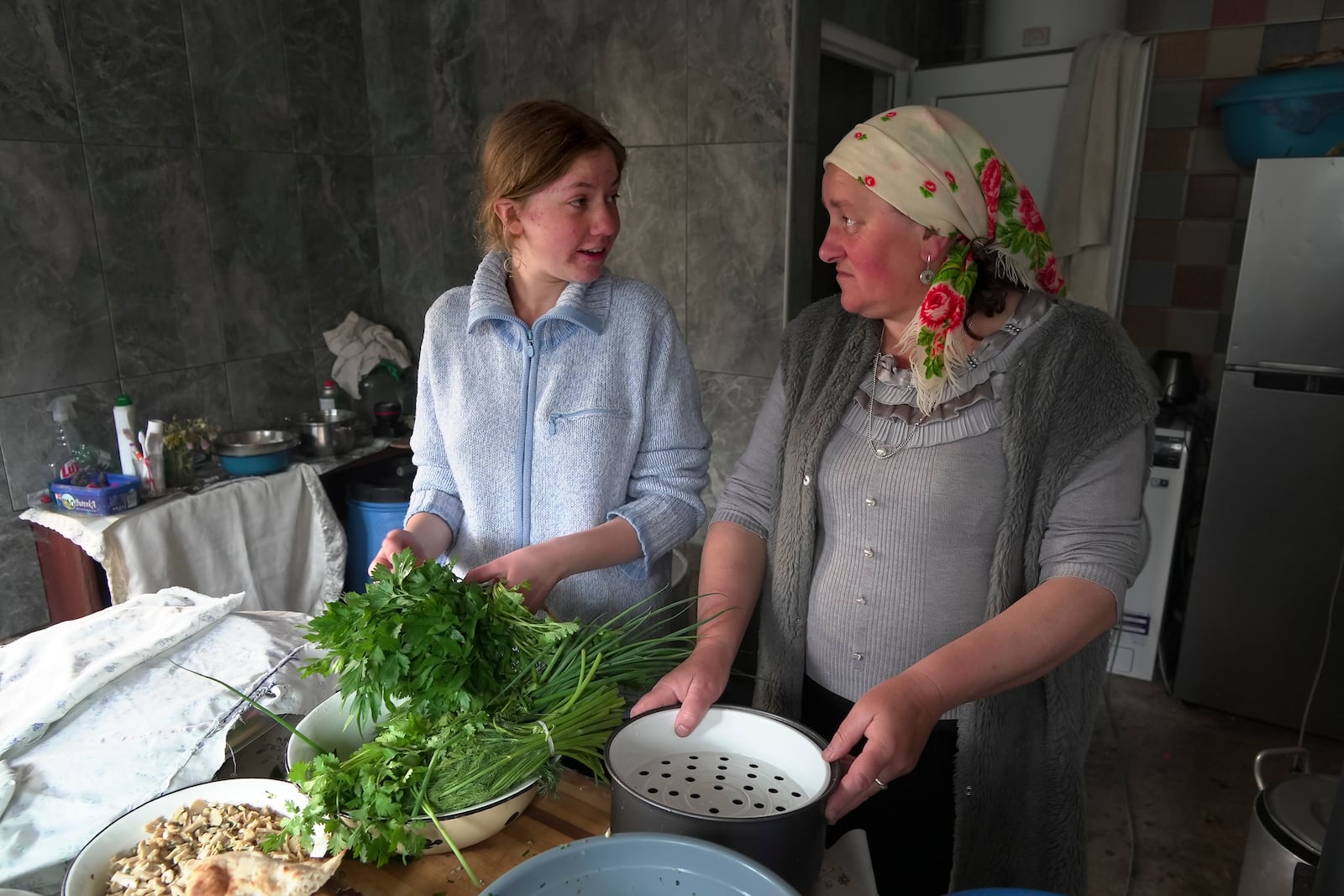 Svetlana Svetlishcheva, left, and her daughter Nina Strukova, right, talk as they cook dinner in their house in the remote mountain village of Orlovka, Georgia, Sunday, May 5, 2024. (AP Photo/Kostya Manenkov)