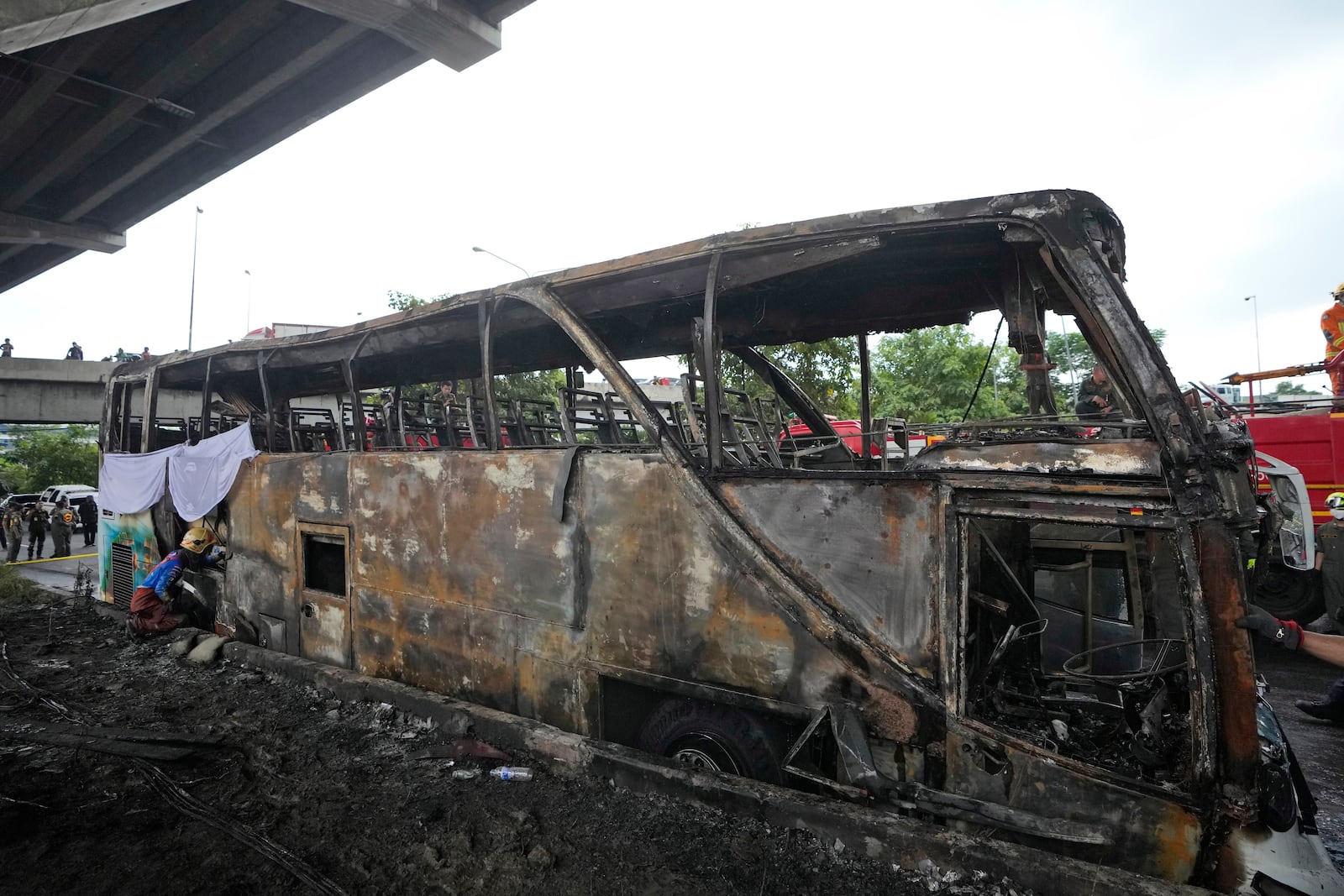 A rescuer inspects a bus that caught fire, carrying young students with their teachers, in suburban Bangkok, Tuesday, Oct. 1, 2024. (AP Photo/Sakchai Lalit)