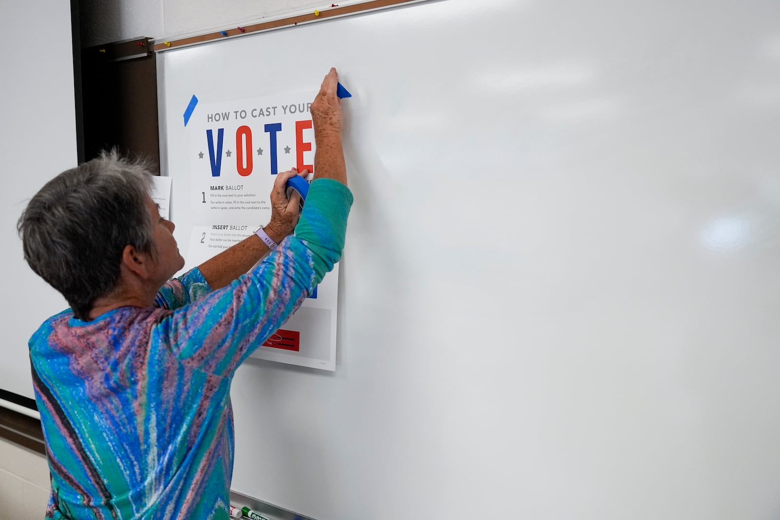 A poll worker hangs up signs at an early in-person voting site at Asheville-Buncombe Technical Community College, Wednesday, Oct. 16, 2024, in Marshall, N.C. (AP Photo/Stephanie Scarbrough)