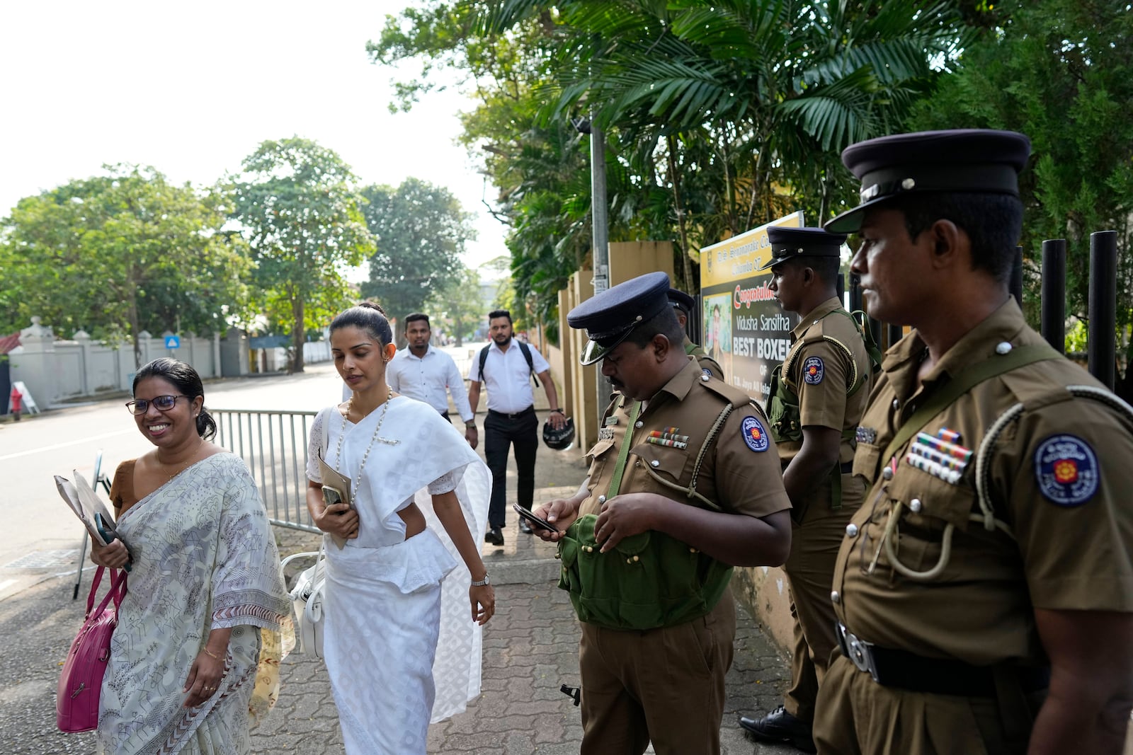 Women election officials walk past security personnel outside a distribution center before collecting polling materials for the upcoming presidential election, in Colombo, Sri Lanka, Friday, Sept. 20, 2024. (AP Photo/Eranga Jayawardena)