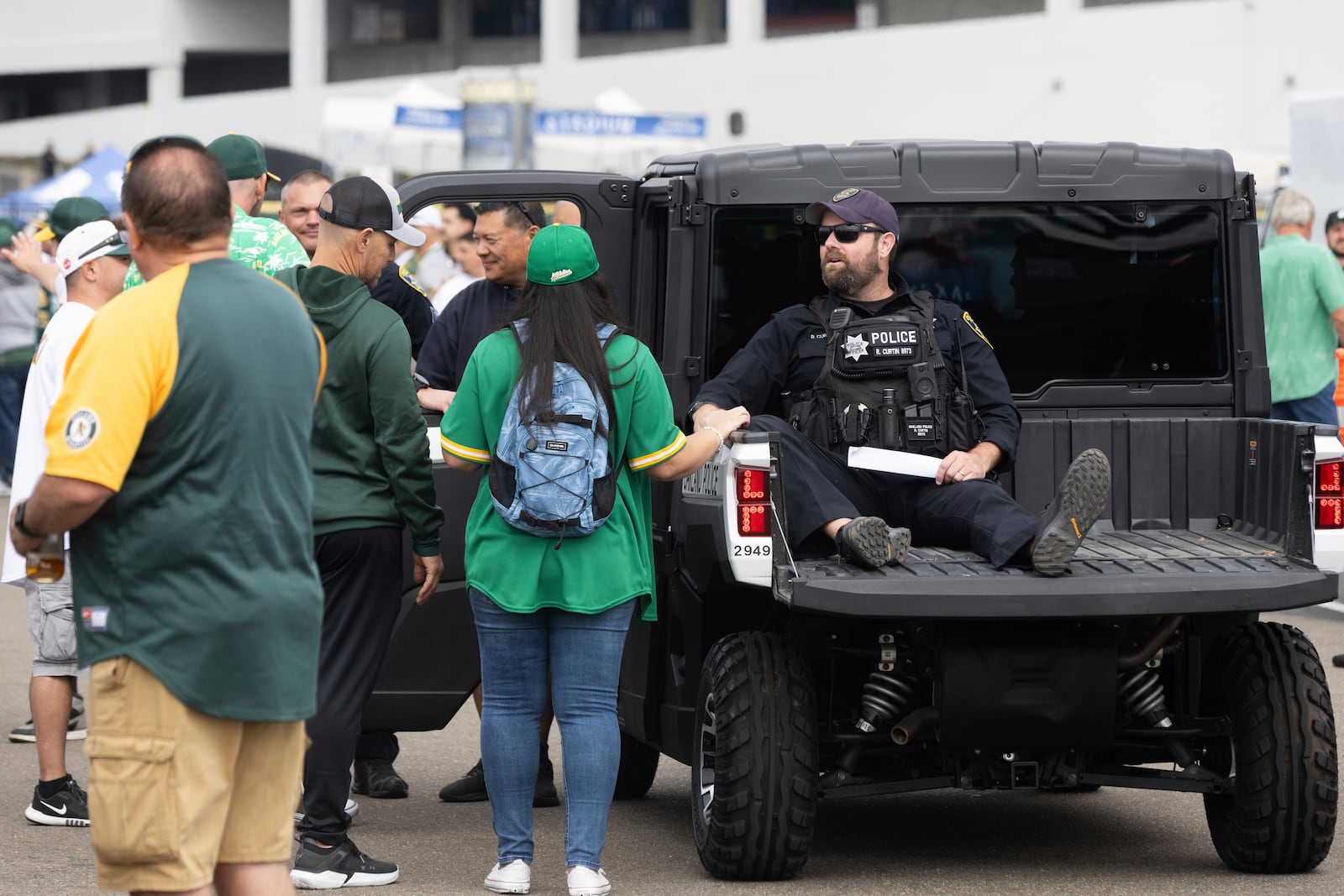 A police officer interacts with fans outside the Oakland Coliseum before a baseball game between the Oakland Athletics and the Texas Rangers Thursday, Sept. 26, 2024, in Oakland, Calif. (AP Photo/Benjamin Fanjoy)