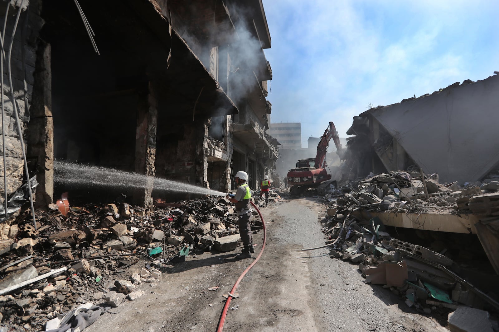 A Hezbollah firefighter hoses down on burned and destroyed shops at a commercial street that was hit Saturday night by Israeli airstrikes, in Nabatiyeh town, south Lebanon, Sunday, Oct. 13, 2024. (AP Photo/Mohammed Zaatari)