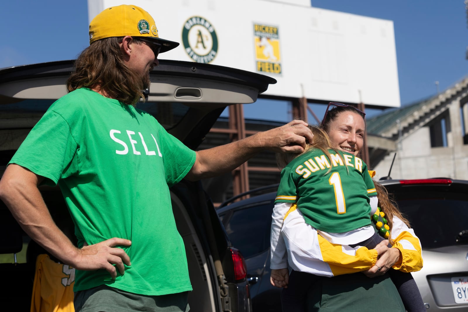 Jacob Sutter, left, stands as Marta Sutter holds their daughter, 3-year-old Summer Sutter outside the Oakland Coliseum before a baseball game between the Oakland Athletics and the Texas Rangers Thursday, Sept. 26, 2024, in Oakland, Calif. (AP Photo/Benjamin Fanjoy)