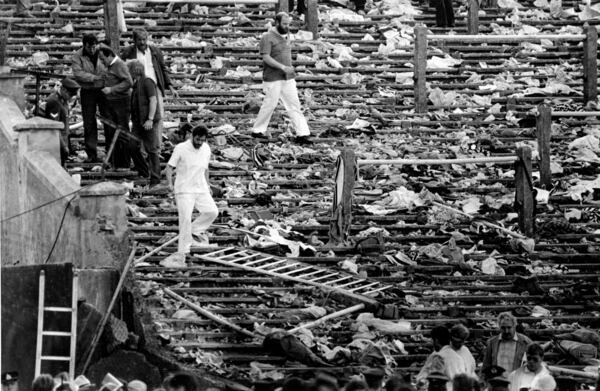 FILE - Shocked spectators walk through the personal belongings of victims littering the stands, after a disastrous clash between rival soccer fans at the European Cup Final at Heysel Stadium in Brussels, Belgium, on May 29, 1985. (AP Photo, File)