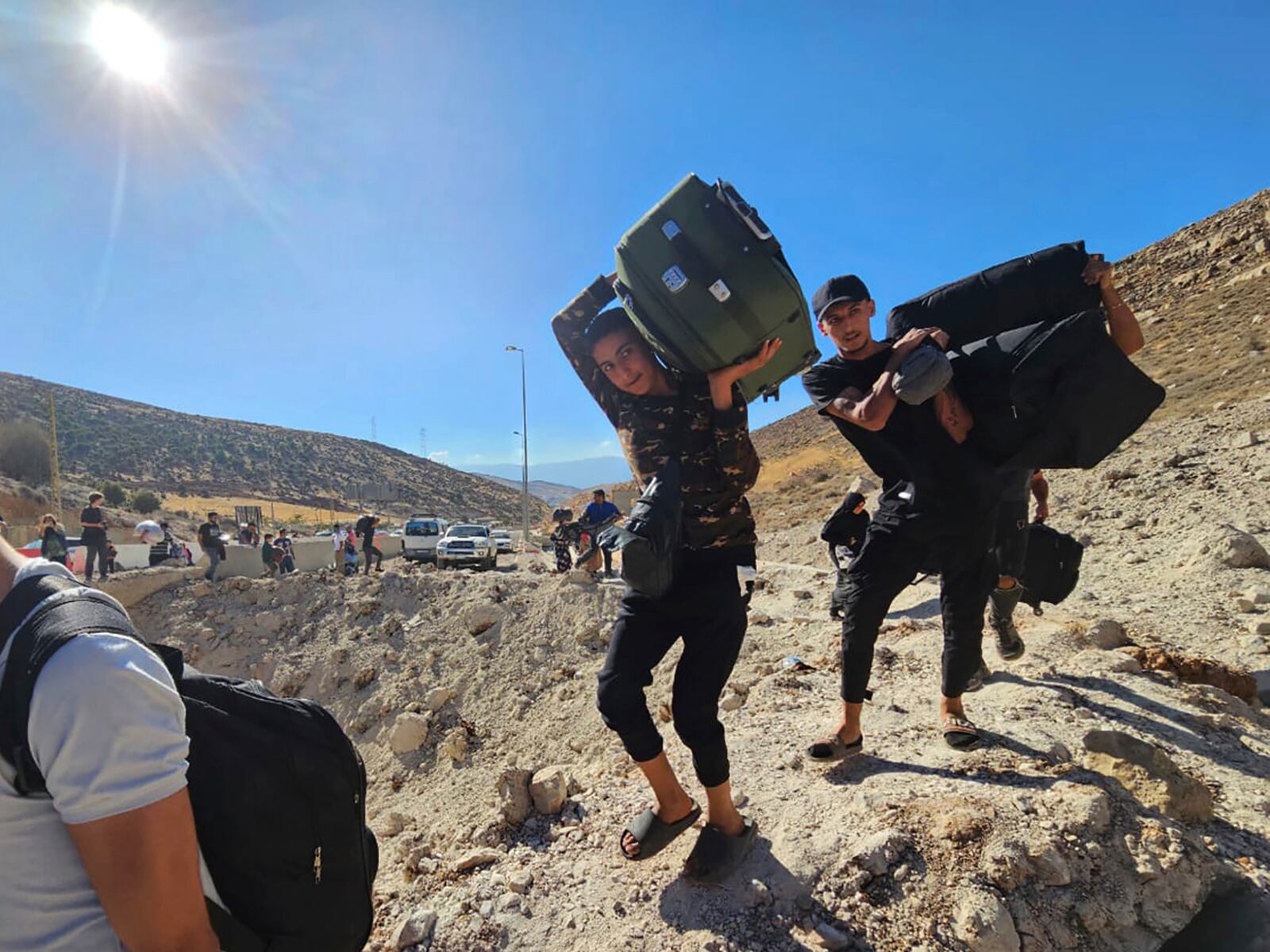 Syrians carry their luggages as they cross on foot into Syria through a crater caused by an Israeli airstrike to cut the road between the Lebanese and the Syrian checkpoints, at the Masnaa crossing, in the eastern Bekaa Valley, Lebanon, Friday, Oct. 4, 2024. (AP Photo/Samer Husseini)