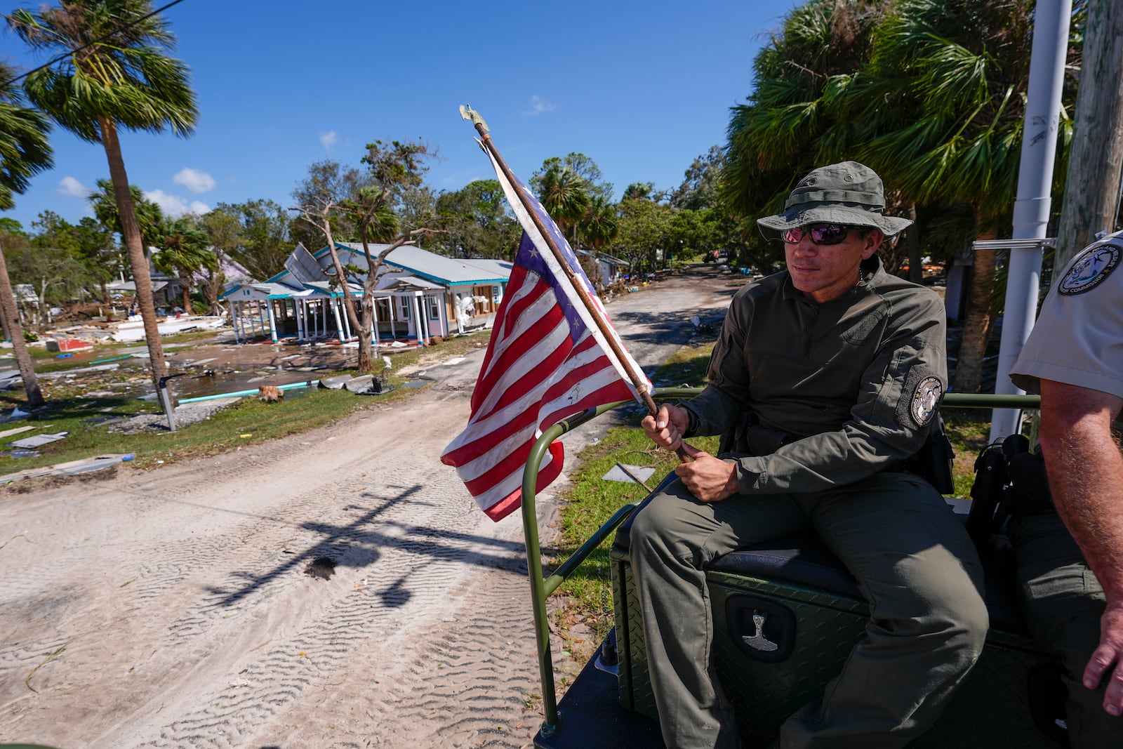 Officer Nate Martir, a law enforcement officer from the Florida Fish Wildlife and Conservation Commission, holds an American flag that was lying on the ground amid debris, while patrolling from a high water capable swamp buggy, in the aftermath of Hurricane Helene, in Cedar Key, Fla., Friday, Sept. 27, 2024. (AP Photo/Gerald Herbert)