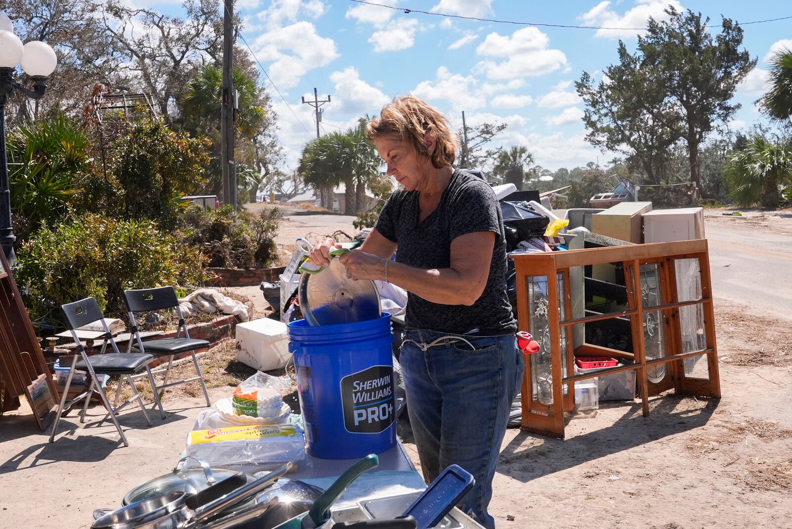 Susan Merritt, of Knoxville, Tenn., tries to clean and salvage pots and pans from her aunt's destroyed home in the aftermath of Hurricane Helene, in Steinhatchee, Fla., Sunday, Sept. 29, 2024. (AP Photo/Gerald Herbert)