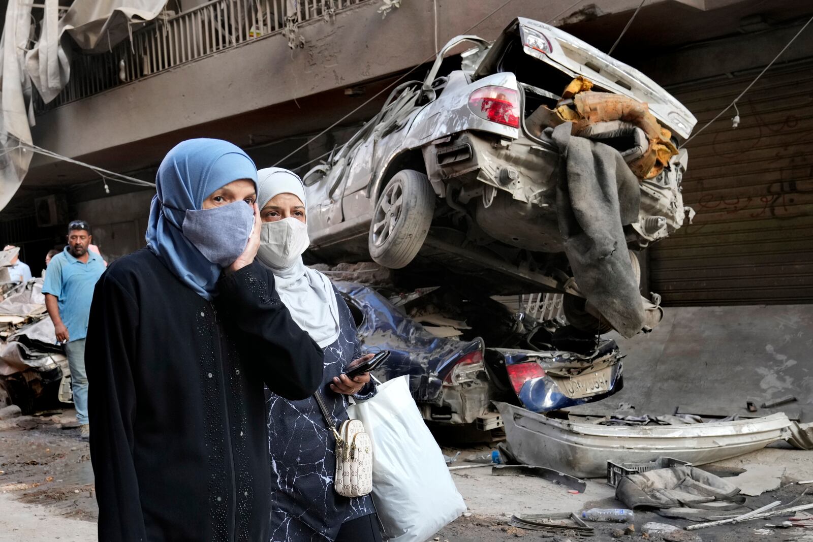 Lebanese women pass next of destroyed cars, at the site of Thursday's Israeli airstrike, in Beirut, Lebanon, Friday, Oct. 11, 2024. (AP Photo/Hussein Malla)